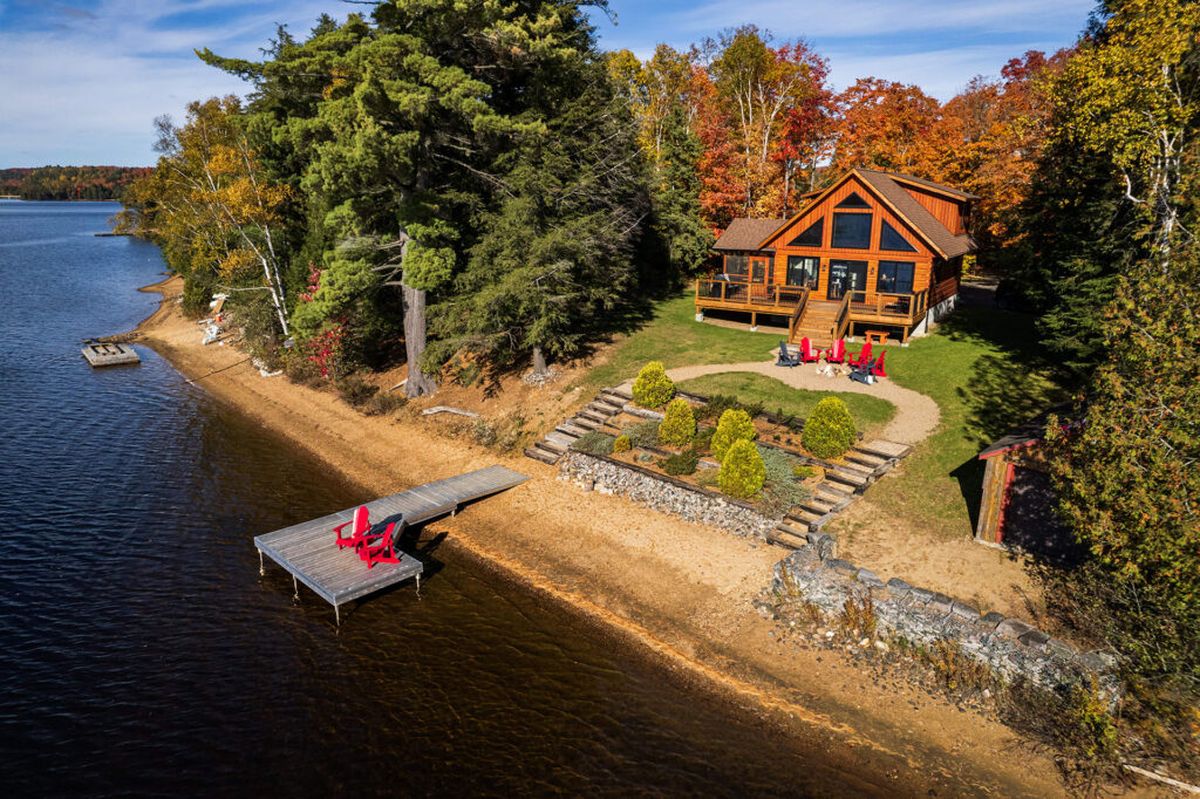 Waterfront cottage on a lake in the Kawarthas surrounded by fall foliage, with a dock and red Adirondack chairs